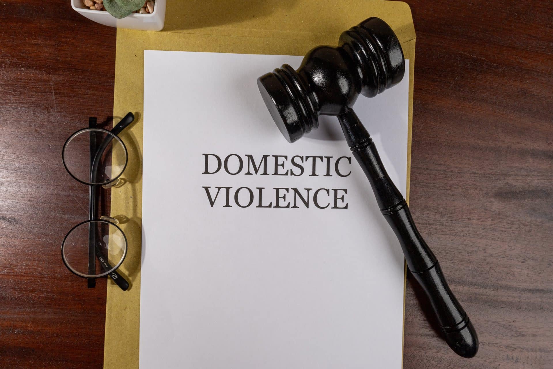 Glasses next to a folder and paper that say domestic violence next to a gavel